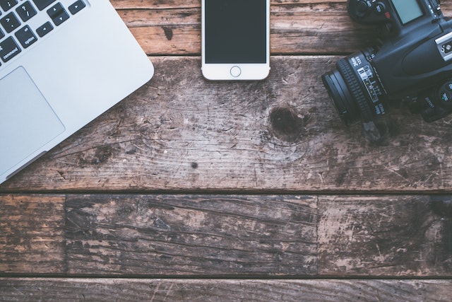 a laptop cellphone and camera on a wooden desk